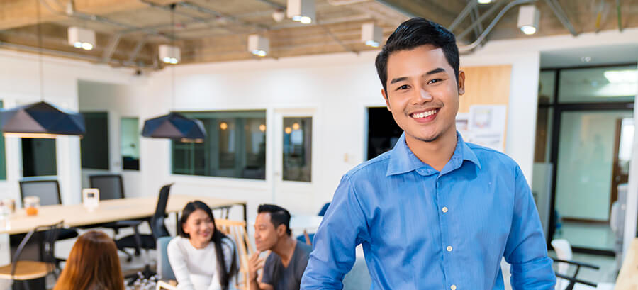 young, smiling man standing in front of coworkers