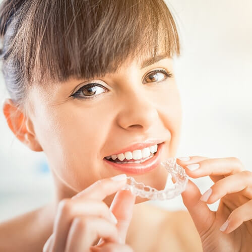 woman inserting clear aligners onto her teeth