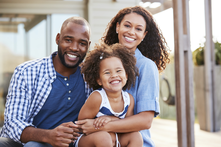 Beautiful Black family of a mom, dad, and their daughter smiling before visiting their family dentist in McKinney, TX