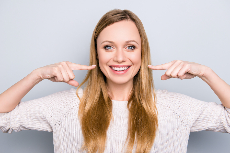 Blonde woman in a white shirt smiles and points to her teeth