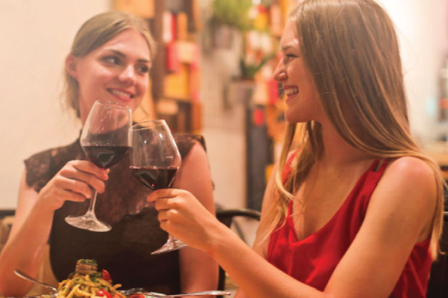 two young women toast with glasses of red wine